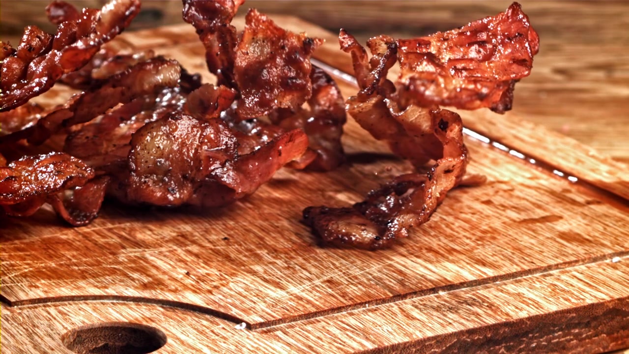 Strisce di pancetta fritta croccante che cadono su un tagliere di legno
