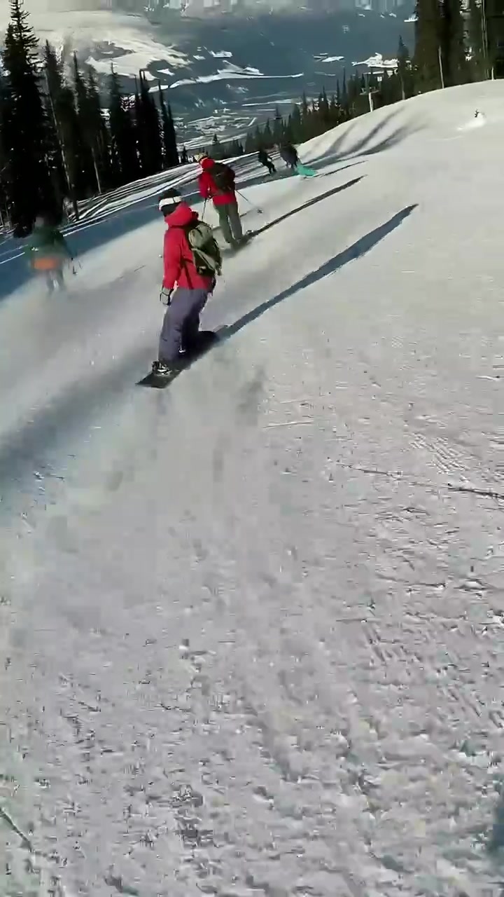 Video verticale: Telecamera che segue uno snowboarder con giacca rossa che scende la pista, rallentando per gli sciatori, con spazio per il testo.