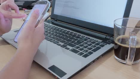 home office desk setup: hands using smartphone with laptop, coffee, smartwatch, lamp, and stationery