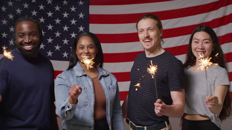 studio portrait shot of multi-cultural group of friends holding sparkler fireworks in front of american flag celebrating 4th july independence day 2