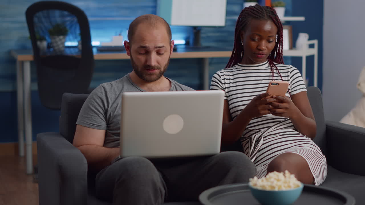 Young interracial couple using technology in living room