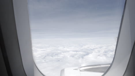 view of the wing and engine of a flying plane aircraft while traveling and dolly out of the window in the cabin with beautiful blue sky and white clouds