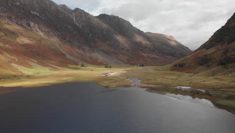 Tirando-Lentamente-Hacia-Atrás-A-Lo-Largo-De-Un-Lago-Oscuro-Para-Revelar-Un-Valle-De-Las-Tierras-Altas-Escocesas-En-Glencoe,-Escocia