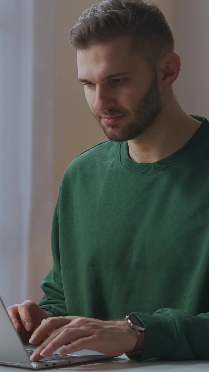 Young Man in Green Sweatshirt Typing on Laptop