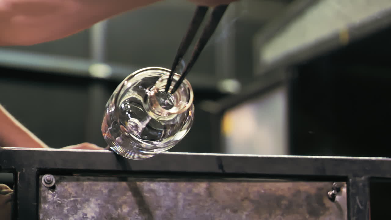 Low angle close up of glass artist spinning a vase, shaping the opening