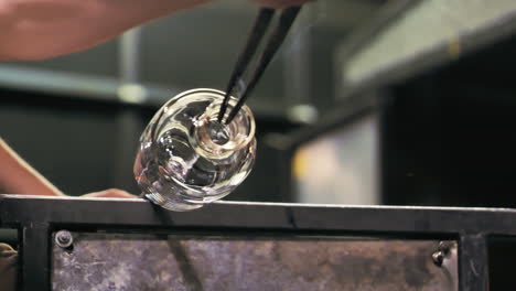 Low-angle-close-up-of-glass-artist-spinning-a-vase,-shaping-the-opening