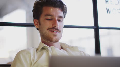 joven blanco trabajando en una computadora portátil, ángulo bajo, cabeza y hombros