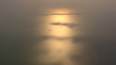 el sol poniente se refleja en el mar con algunos parches de sombra proyectados por las nubes filmadas desde lo alto