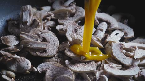 beaten eggs poured onto sliced mushrooms cooking in a pan