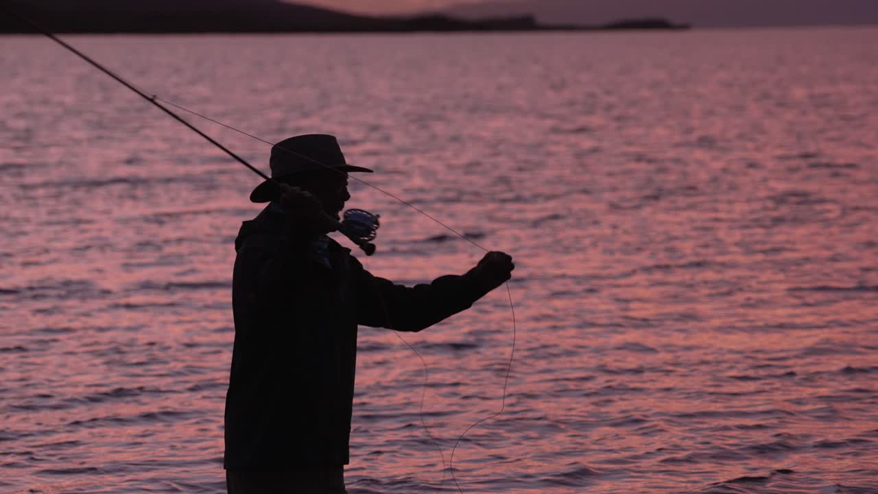 un pescador con mosca en silueta lanza su carrete al atardecer en molokai, hawaii
