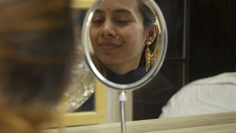 young beautiful asian woman looking at mirror wearing 18k huid certified gold earrings