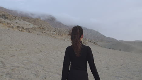 Close-up-of-the-steps-taken-by-a-woman-dressed-in-black-while-walking-through-a-desert-in-the-afternoon-with-a-cloudy-sky