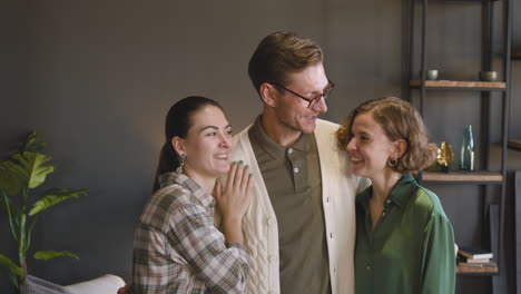 Group-Of-Three-People-Posing-And-Smiling-At-Camera-While-Standing-In-A-Modern-Living-Room-At-Home-1