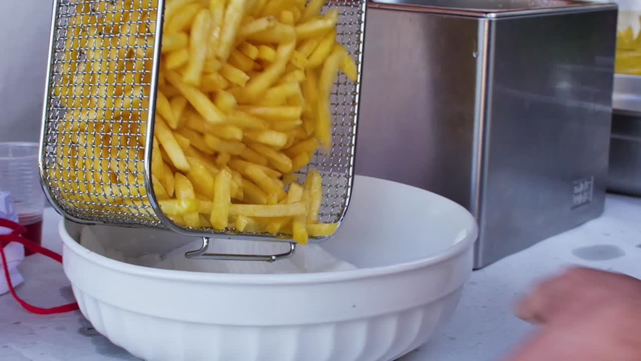 Sprøde, friturestegte pommes frites serveres fra en friturekurv i en hvid serveringsskål.