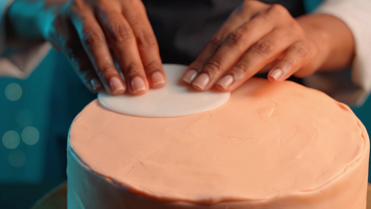 Skillful Baker Applying Fondant to Smoothly Decorate a Cake with Precision and Care in a Beautifully Lit Kitchen Setting