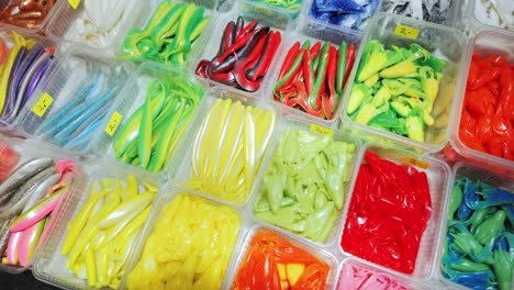 multicolored soft lures stacked in boxes at outdoor angling accessories market