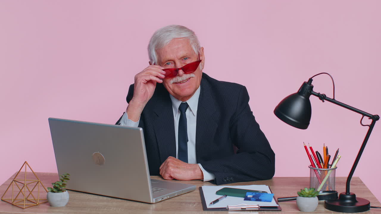 고위 사업가는 엄지손가락을 올리고, 동의하고, 승인하고, 좋은 소식을 좋아합니다. 분홍색 사무실에서 노트북을 사용합니다.