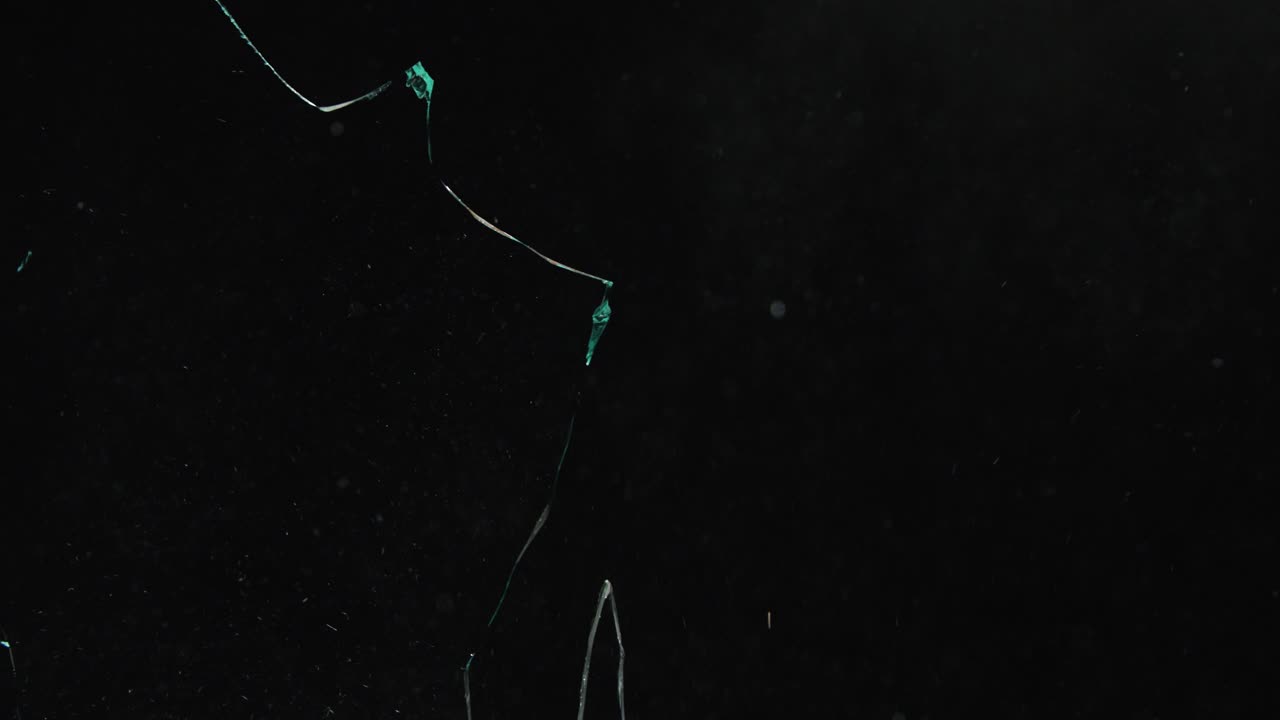 Glass shattering with small particles flying against black. Dynamic breaking effect, abstract destruction, impact for compositing or intros