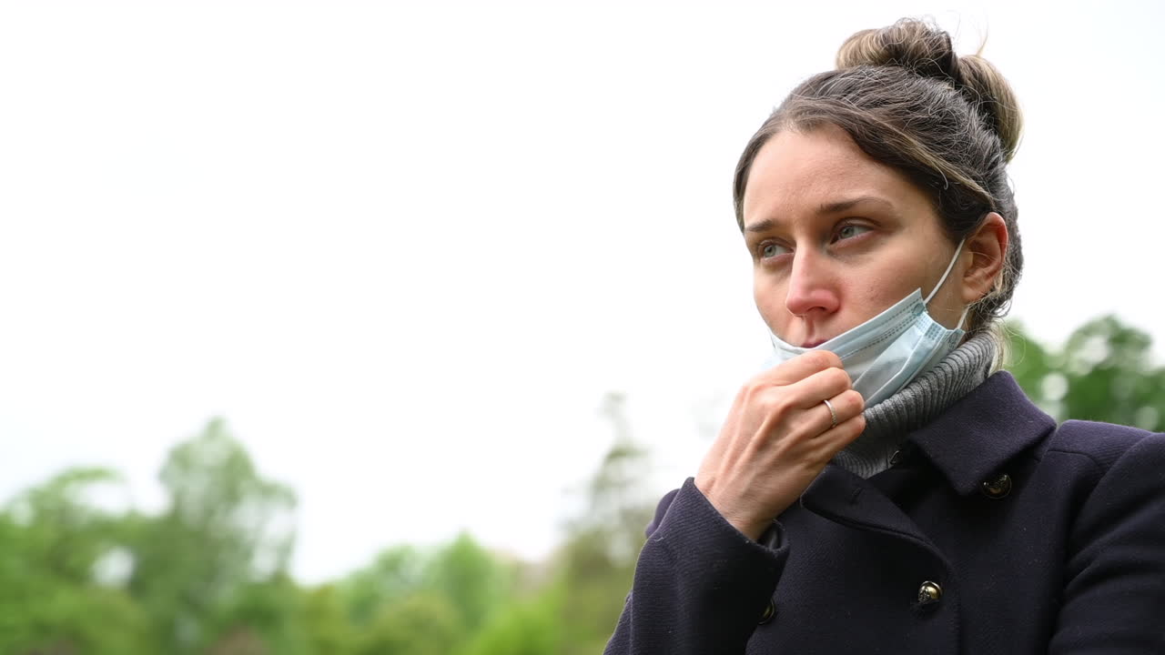 Woman sneezing in a park while holding a tissue, surrounded by green trees