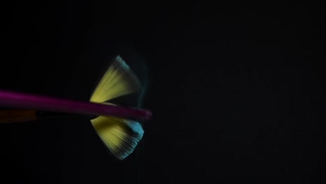 slow motion of a make up brush with blue powder explosion and burst on black background