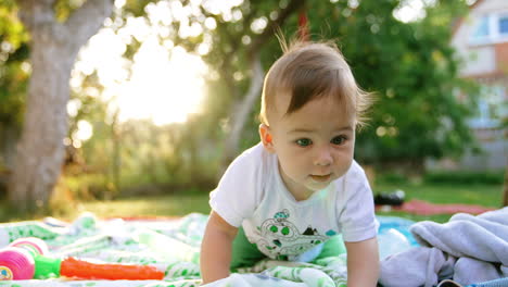 nice cute toddler crawling by the blanket on the ground. baby spending time outdoors in summer. close up. blurred backdrop.