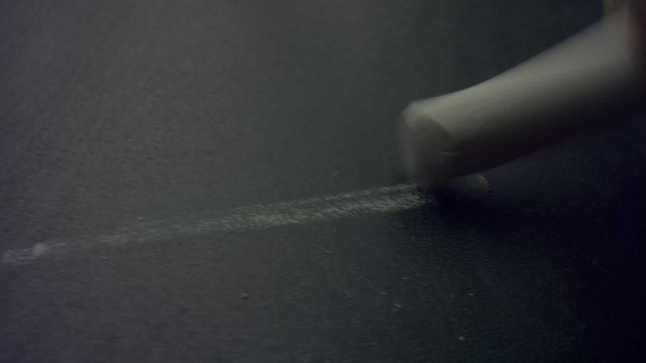 Woman hand holding piece of chalk. Macro of chalk drawing line on blackboard
