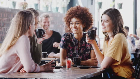 Vier-Junge-Freundinnen-Treffen-Sich,-Sitzen-Am-Tisch-Im-Café-Und-Unterhalten-Sich