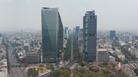 Drone-Volando-Hacia-Adelante-Desde-El-Parque-De-Chapultepec-Entre-Altos-Y-Modernos-Edificios-De-Oficinas-En-La-Amplia-Avenida-Paseo-De-La-Reforma.-Ciudad-De-México,-México.