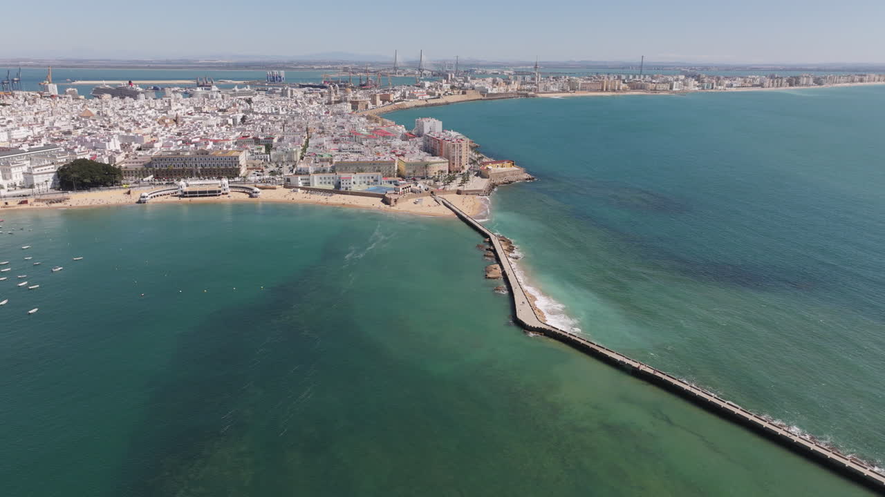 Vista aerea da drone della città vecchia di Cadice e dell'area di La Caleta con frangiflutti e spiagge che si estendono nell'Oceano Atlantico. Paesaggio urbano costiero storico sotto cieli azzurri e limpidi in Andalusia, Spagna, Europa
