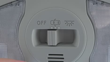 a white caucasian hand flipping the switch of an overhead light in a new car