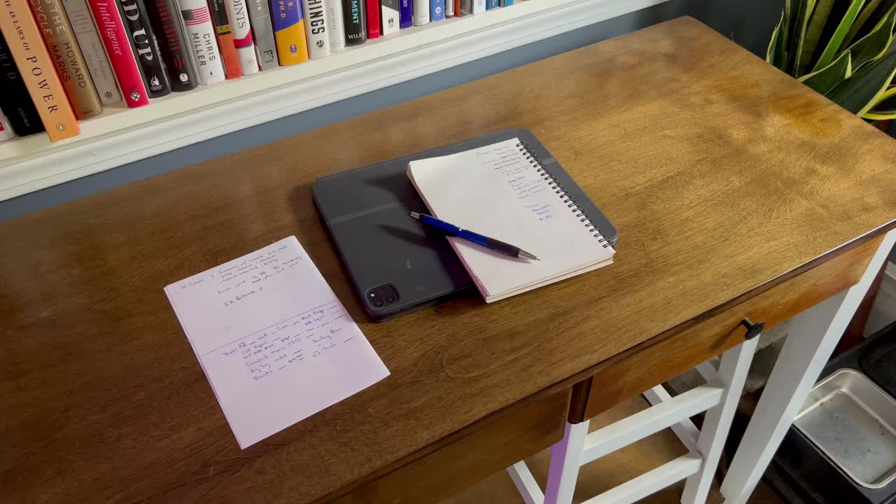 List, notes, tablet, and pen on coffee table with background of books