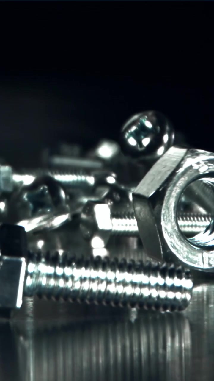 Primo piano di elementi di fissaggio metallici che cadono su una superficie riflettente