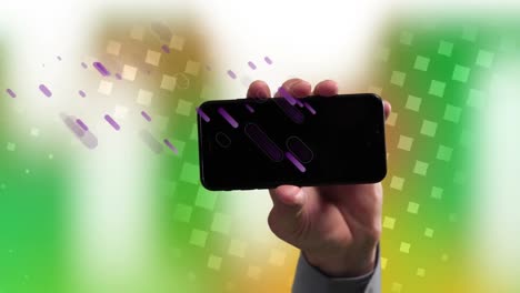 animation of purple shapes falling over hand of caucasian man holding smartphone with copy space