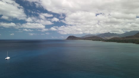 Slow-moving-aerial-flying-towards-the-mountains-over-the-ocean-with-a-boat-in-the-scene