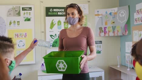 grupo de niños con máscaras faciales poniendo artículos de plástico en contenedores de reciclaje