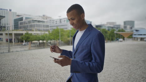 Smiling-young-man-holding-credit-card-and-smartphone-outdoor.