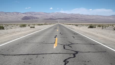 carretera calefactada agrietada que cruza el valle de la muerte, desierto de mojave, california, plataforma rodante delantera en toma