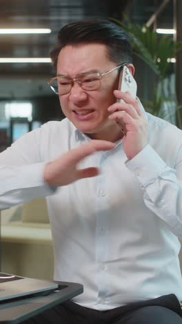 angry young businessman ceo in shirt making smartphone online conversation call in office lobby