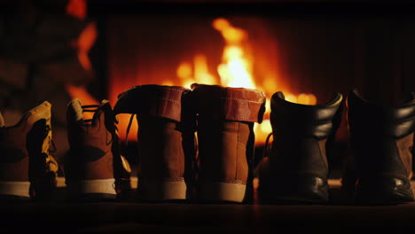 a few pairs of winter shoes are drying near the fireplace where the fire is on