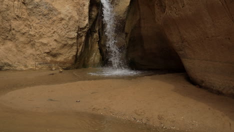 Small-waterfall-cascading-into-a-serene-pool-within-the-oasis-of-Tozeur,-Tunisia,-surrounded-by-rugged-cliffs