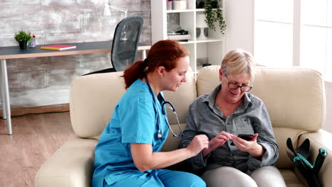 nurse in retirement home sitting on the couch helping elderly woman to use a smartphone