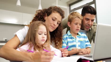 niños lindos dibujando en la mesa con sus padres y usando computadora portátil