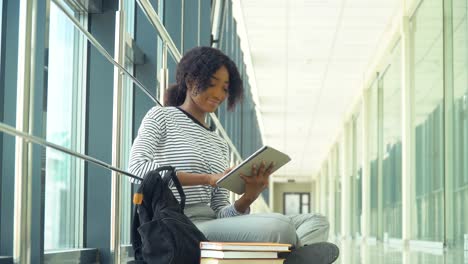 estudiante afroamericana sentada en el suelo con una tableta en la universidad. nueva instalación de educación moderna y totalmente funcional. concepto de educación en línea