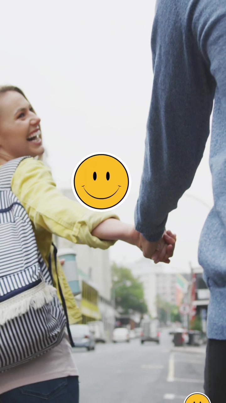 Animación de emojis digitales flotando sobre pareja caucásica feliz caminando y tomados de la mano
