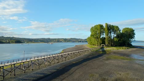 vista aérea siguiendo el muelle a la isla de aucar, día soleado en chiloe, chile