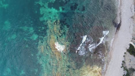 rocky shoreline with crystal clear water meeting a small pebble beach, aerial view