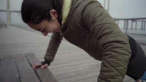 una mujer joven riendo haciendo flexiones desde un banco de madera al aire libre