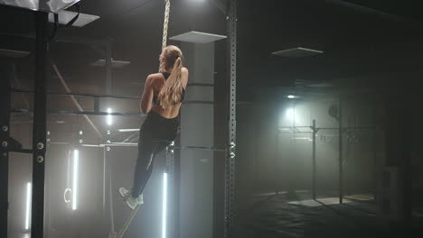 full length wide angle shot of a woman performing rope climbs at the gym. athletics healthy composition. cross fitness. determined athletic woman moving up the rope in a gym.