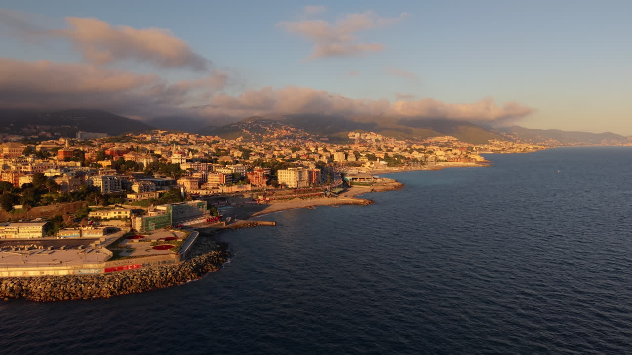 Drone che vola sul mare verso la costa di Genova con montagne al tramonto.