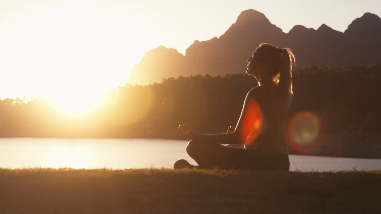 mujer meditando haciendo yoga junto a un hermoso lago y montañas al atardecer